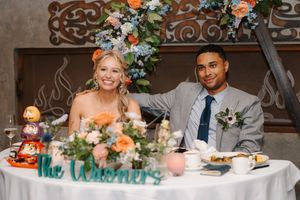 A couple sits at their wedding reception table decorated with peach and white floral arrangements and personalized decor.