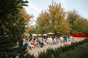 Guests seated in white chairs at an outdoor wedding ceremony with autumn trees displaying golden foliage.