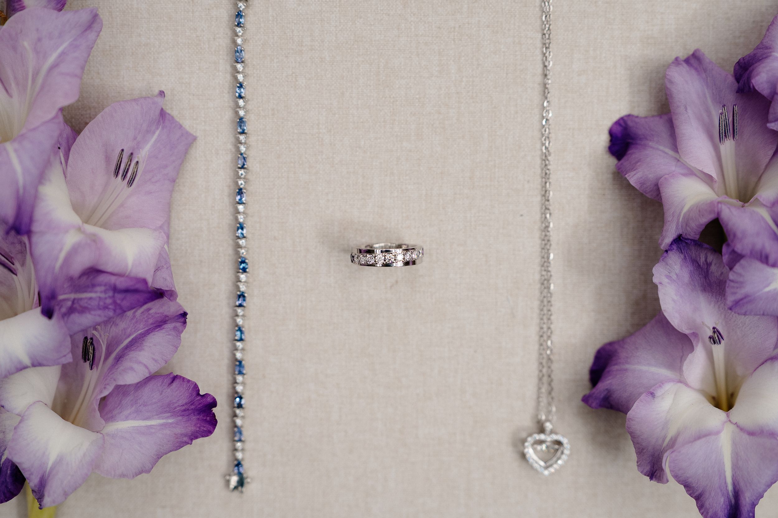 Purple gladiolus flowers bloom in a row against a soft neutral background with delicate beaded decorations.