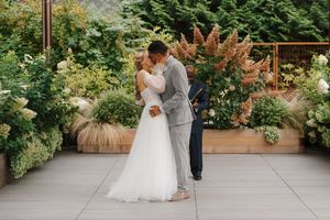 A couple shares a romantic moment on an outdoor patio surrounded by lush greenery and wooden pergolas.