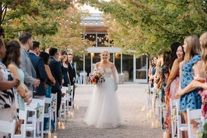An outdoor wedding ceremony with white chairs lining a path surrounded by autumn trees.