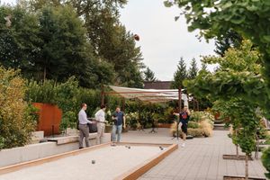 Outdoor bocce ball court with wooden benches and landscaping along a paved walkway.