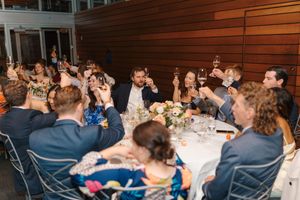 Wedding reception guests seated at tables share laughter and conversation during an indoor celebration.