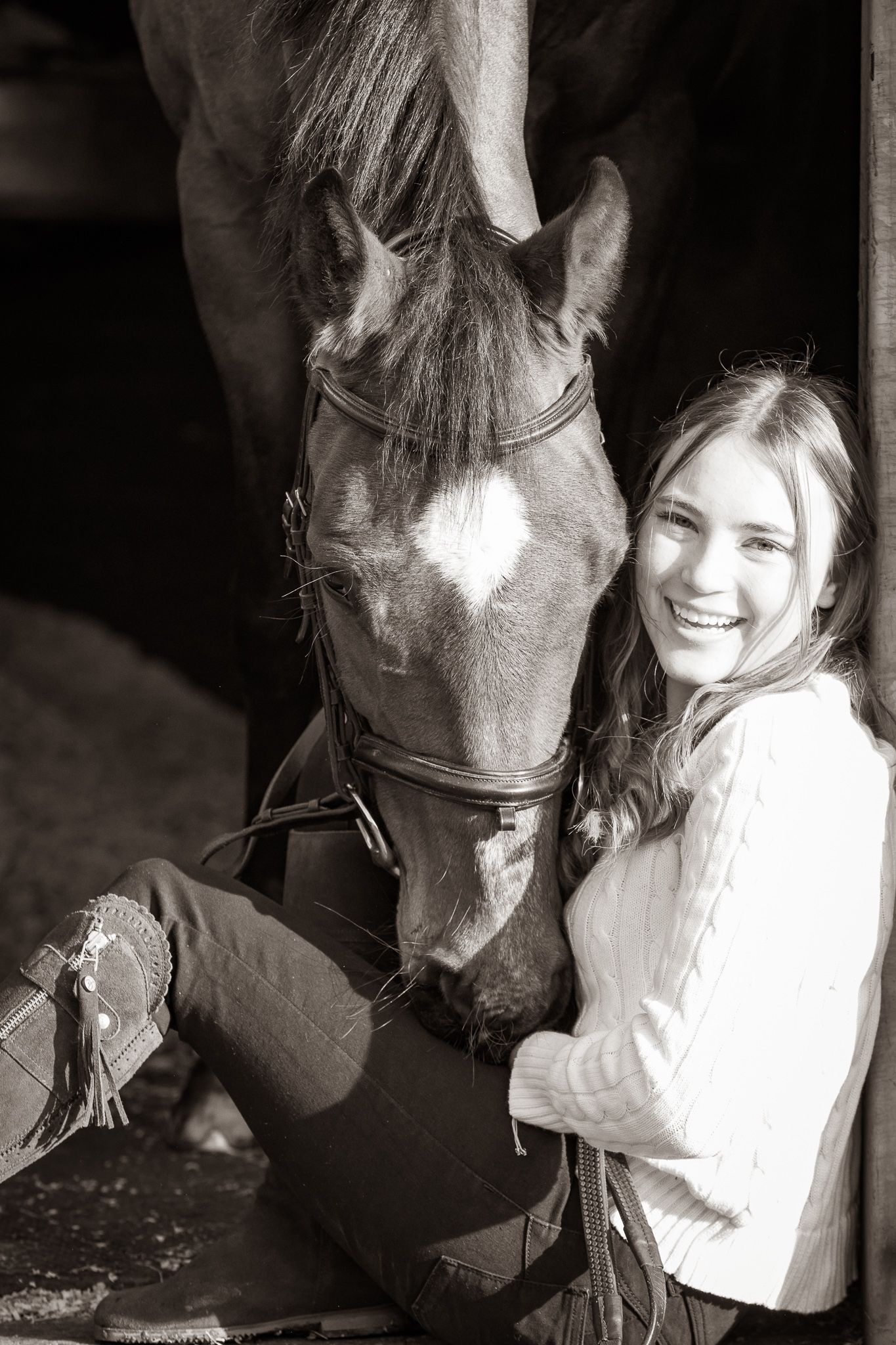 A black and white photograph shows a person sharing a tender moment with a dark horse in a stable.