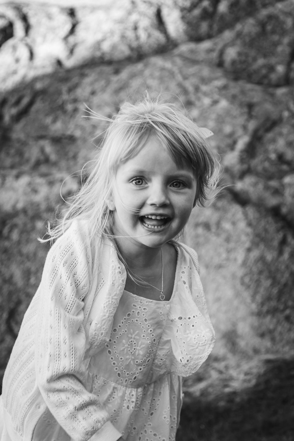 Black and white portrait series of a young child in a white lace dress against a natural outdoor background.