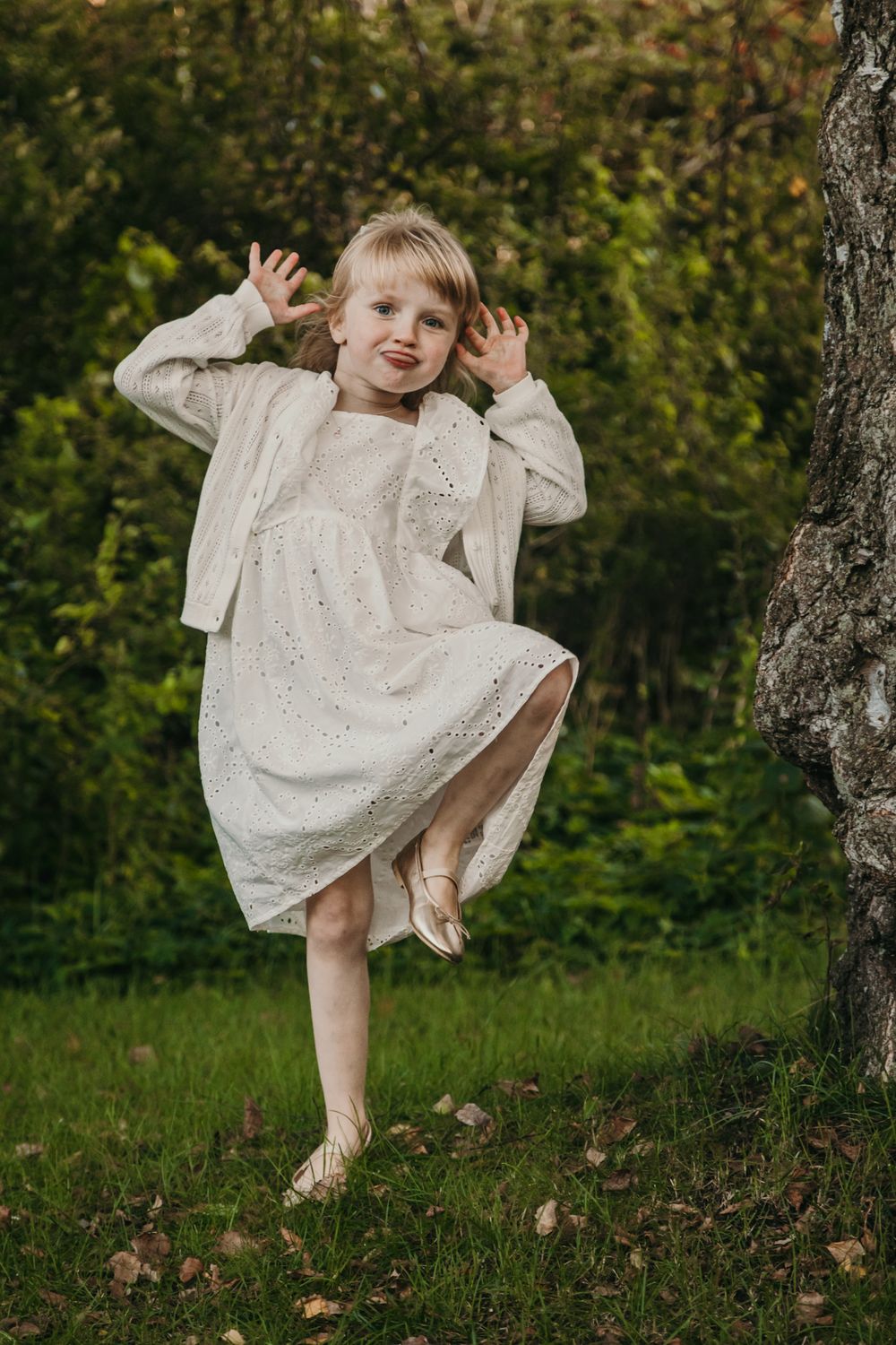 A child in a white eyelet dress twirls and plays under a tree in a series of connected outdoor photos.