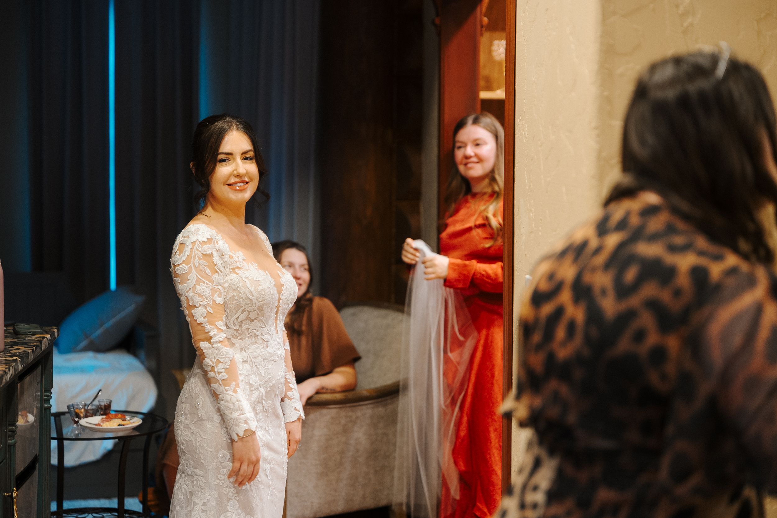 Bride in a lace wedding dress getting ready with her bridal party in a dressing room.
