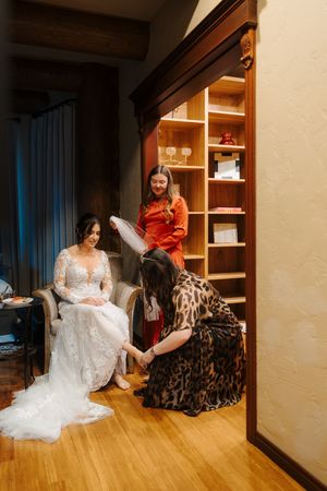 A wedding dress is being fitted and arranged in a dressing room with wooden floors and built-in storage shelves.