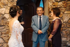 Wedding guests share emotional reactions during a ceremony against a rustic stone wall backdrop.