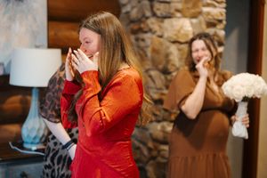Emotional wedding guests wiping tears during ceremony in front of stone wall interior.