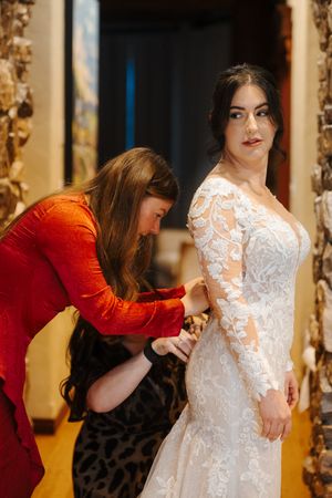 A person in a red top makes adjustments to a white lace wedding dress during a fitting session.