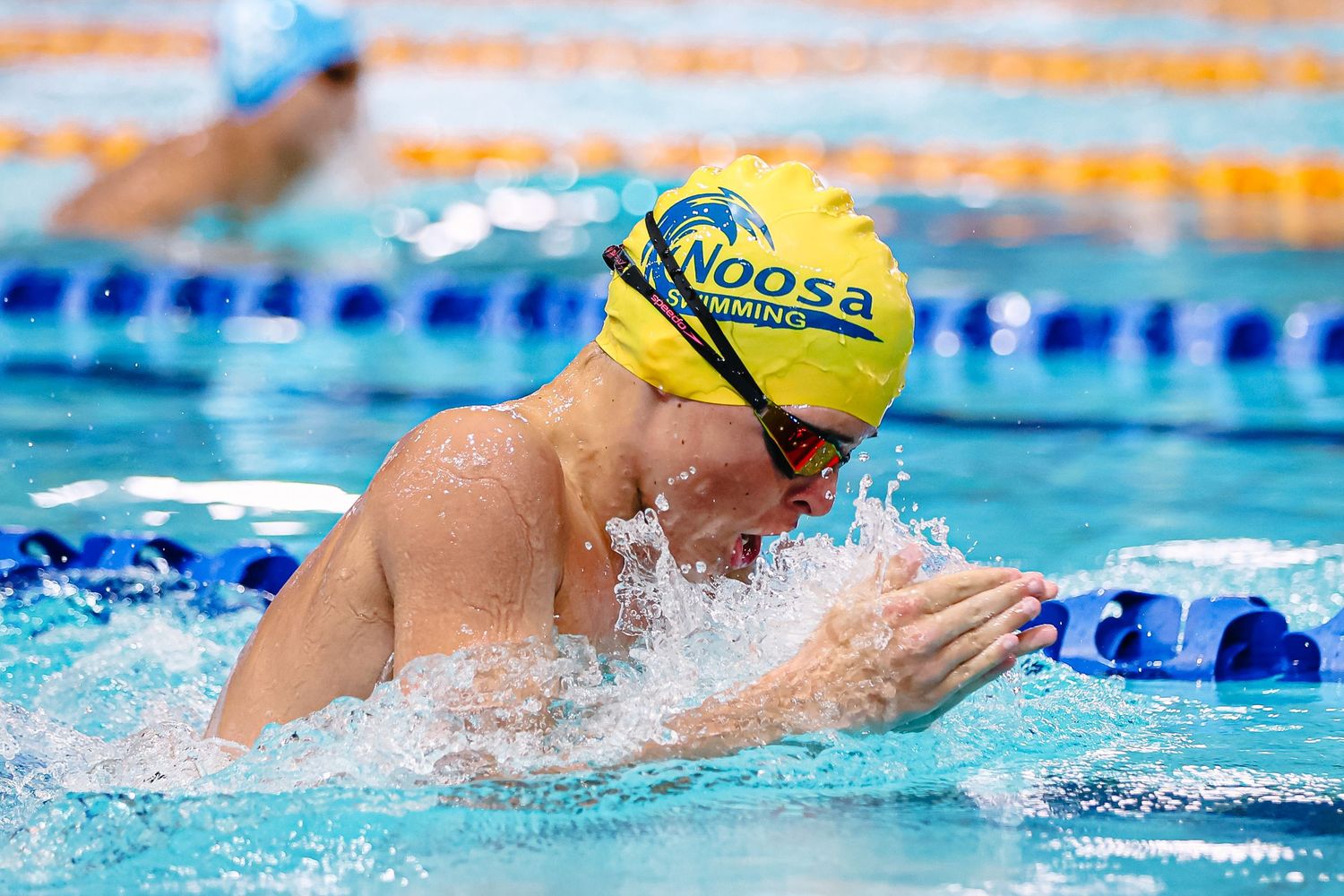 Competitive swimmer performs backstroke in blue pool water with green lane dividers during race.