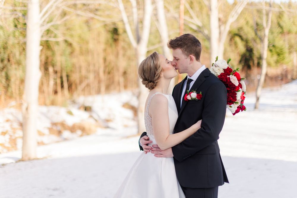 A couple shares a romantic moment in winter, with the bride in white and groom in black against a snowy backdrop.