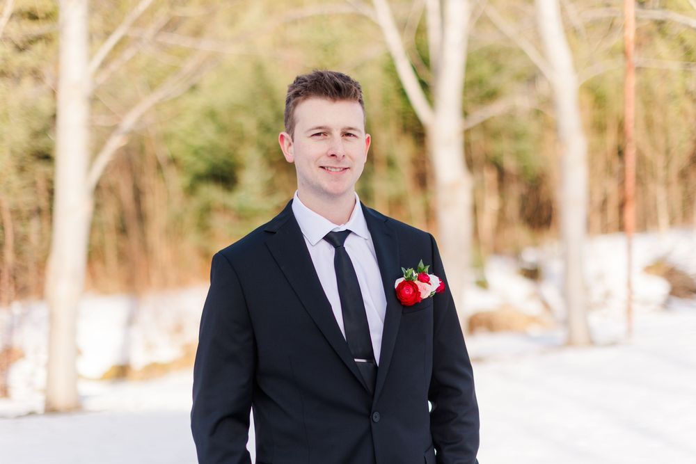 A wedding party poses in the snow wearing formal black attire with red accents and winter accessories.
