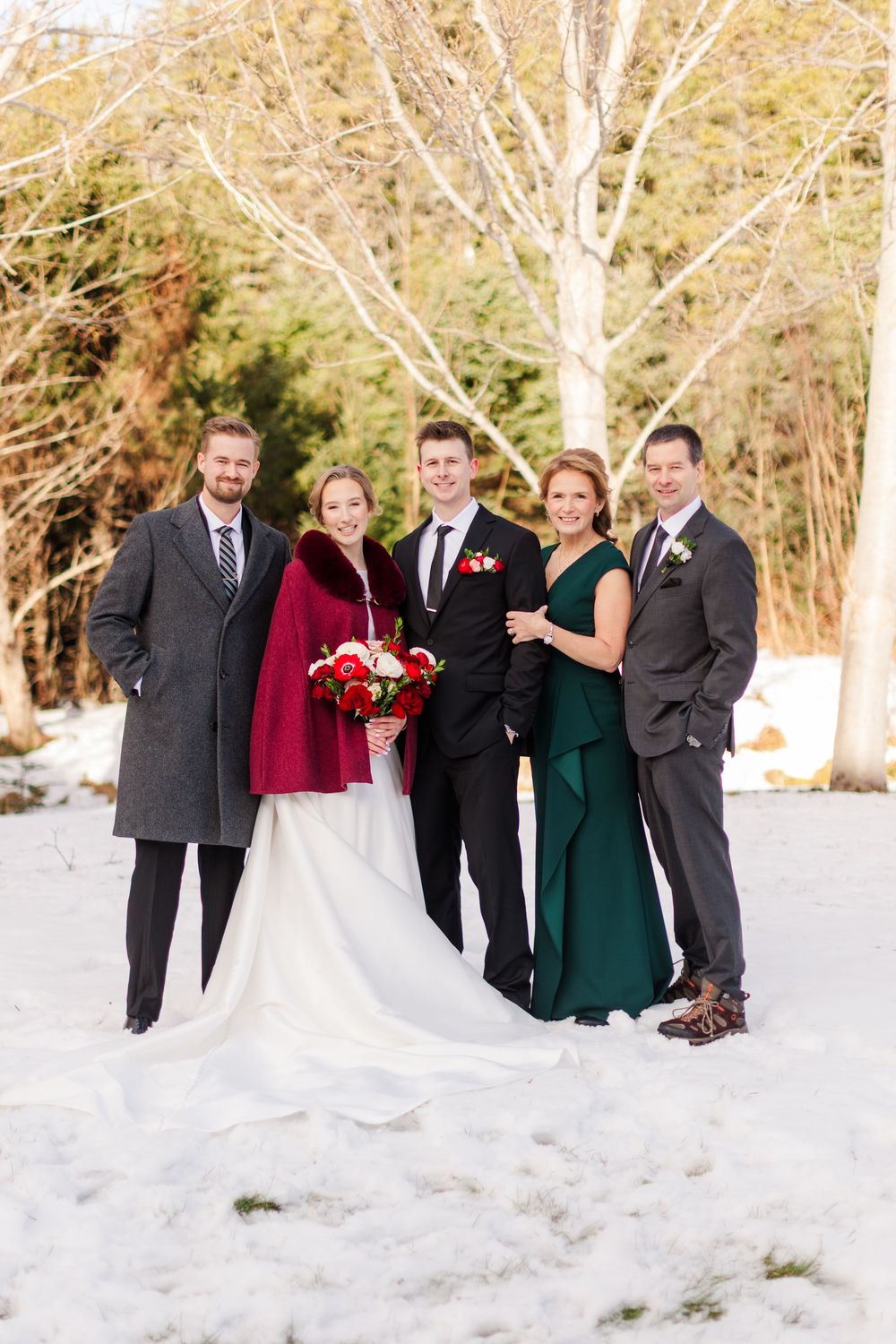 Wedding party poses playfully in a snowy winter landscape with bare trees and white ground.