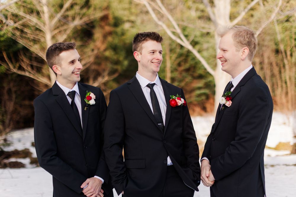 Groomsmen in black suits share laughs and candid moments in a winter setting.