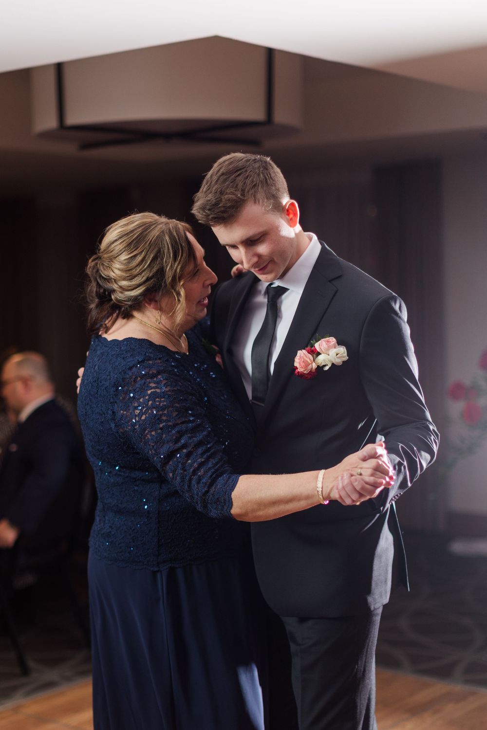 A couple dances together at a formal event, with the woman wearing a navy sequined dress and the man in a black suit.