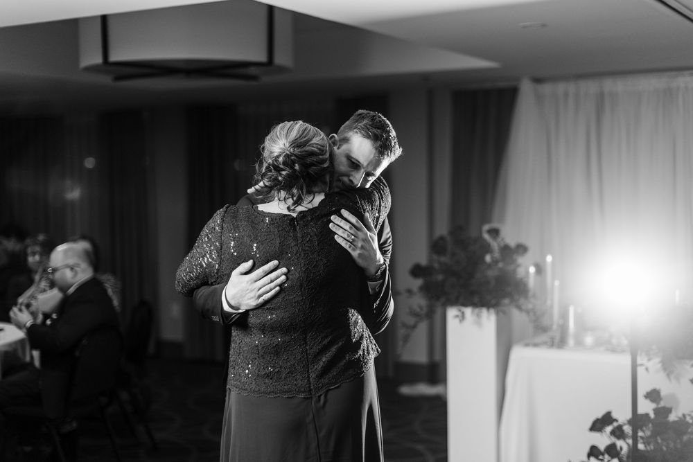 A couple embraces during their first dance at a wedding reception in a dimly lit ballroom.
