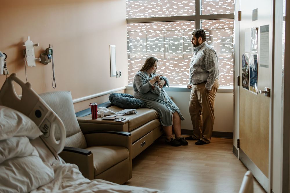 A couple shares a tender moment in a hospital room with their newborn.