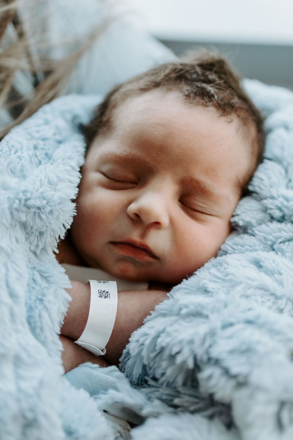 Peaceful newborn sleeping on soft blue blanket with hospital ID bracelet.