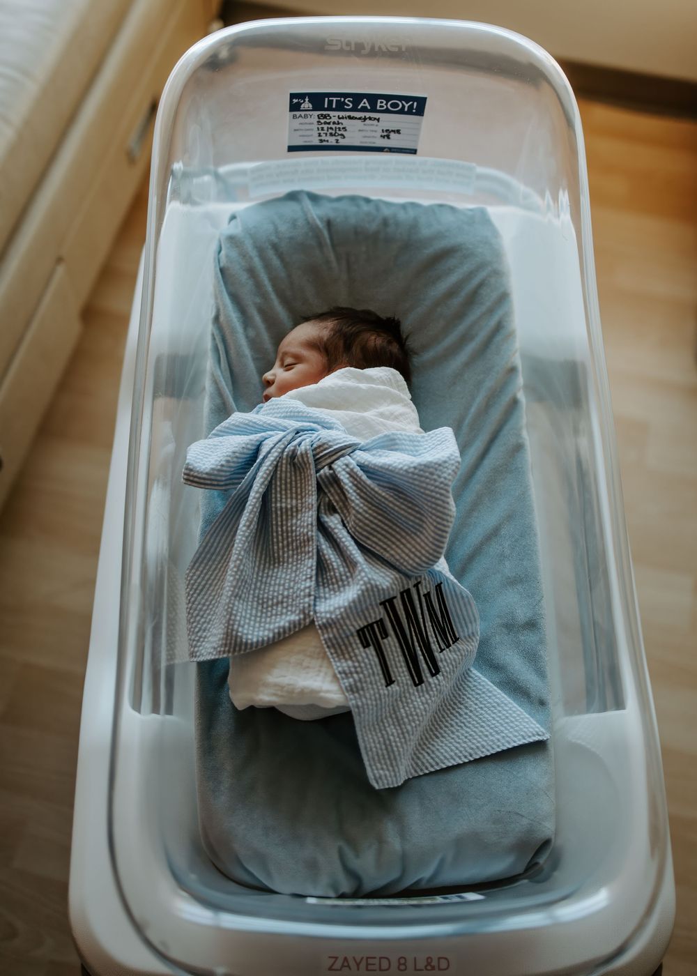 A sleeping newborn baby lies bundled in a hospital bassinet with blue bedding.