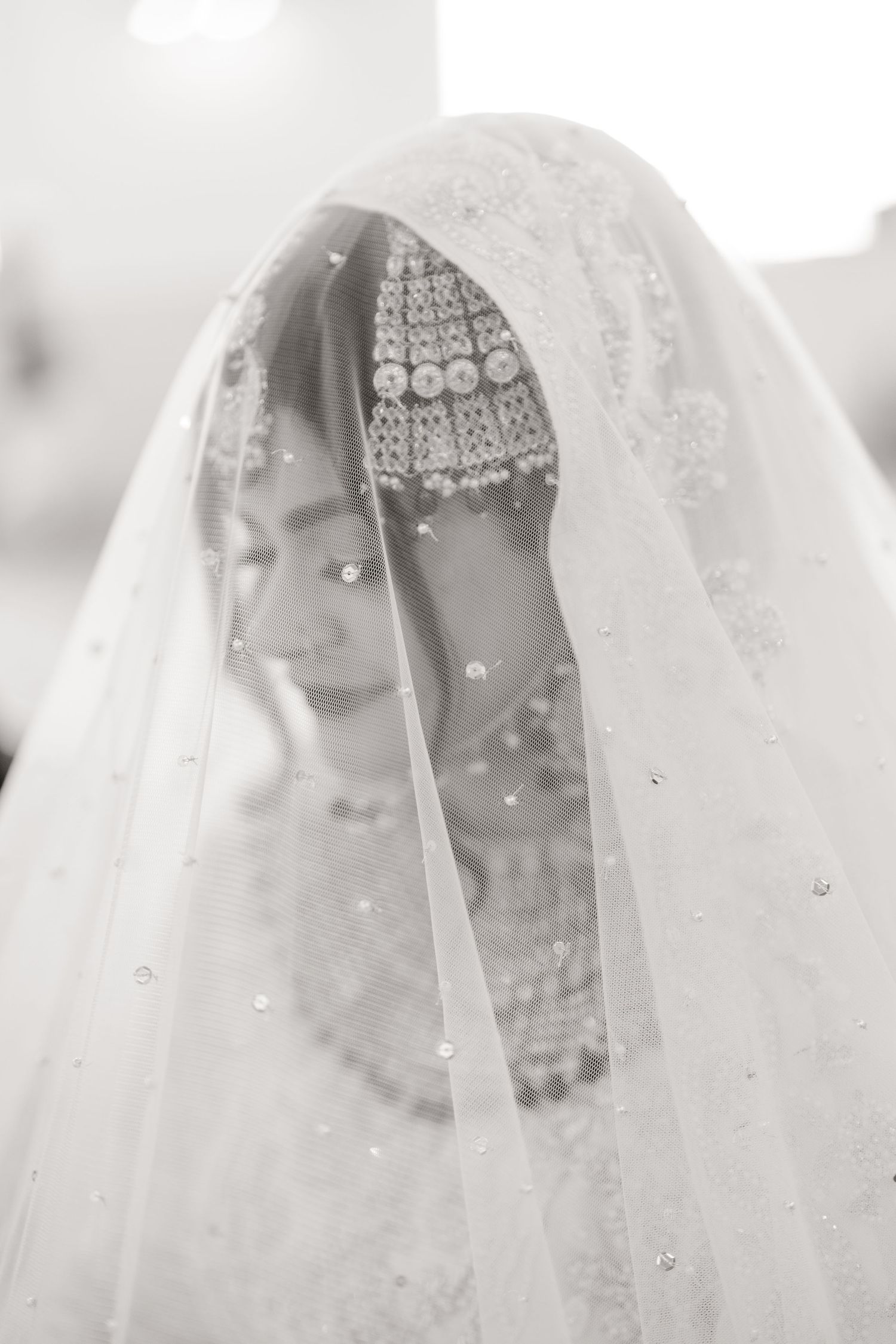 Black and white portrait of South Asian bride wearing ornate jewelry beneath embellished white wedding veil.