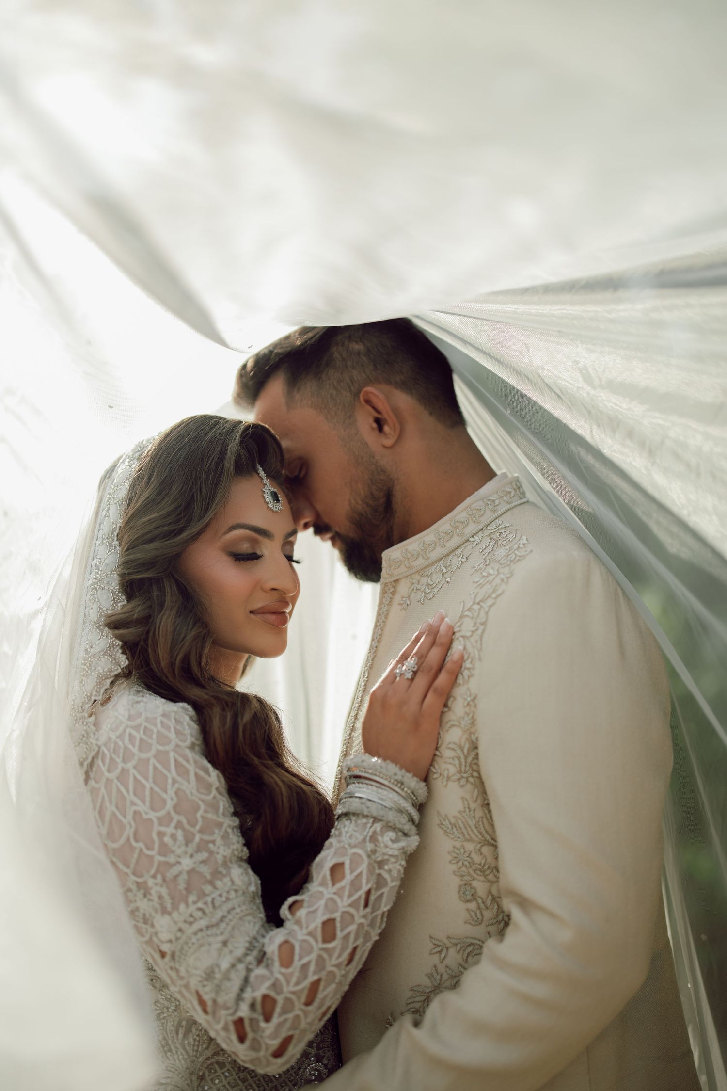 Black and white portrait of South Asian bride wearing ornate jewelry beneath embellished white wedding veil.