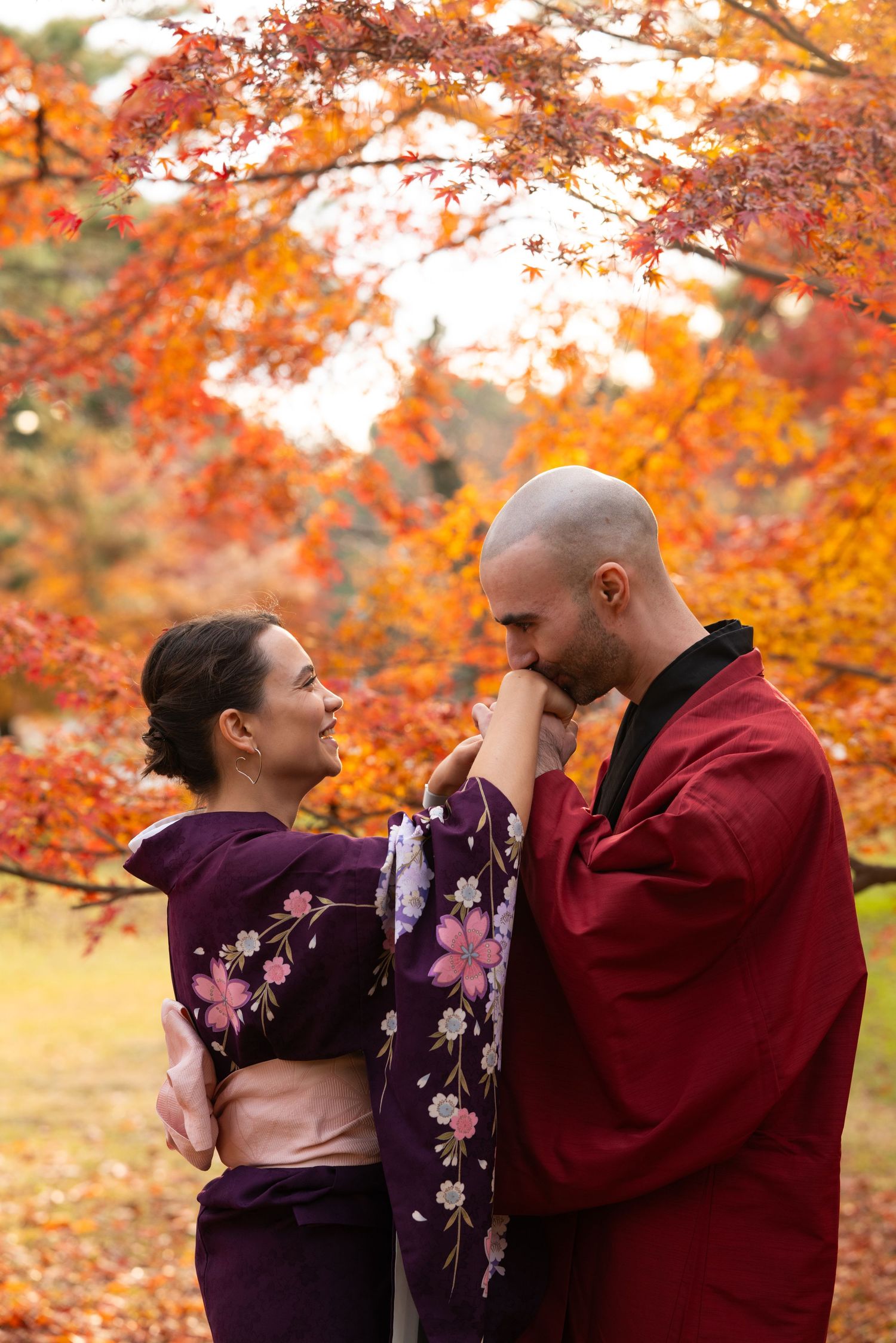 Couple in traditional Japanese kimono sharing a romantic moment under vibrant red autumn maple trees.