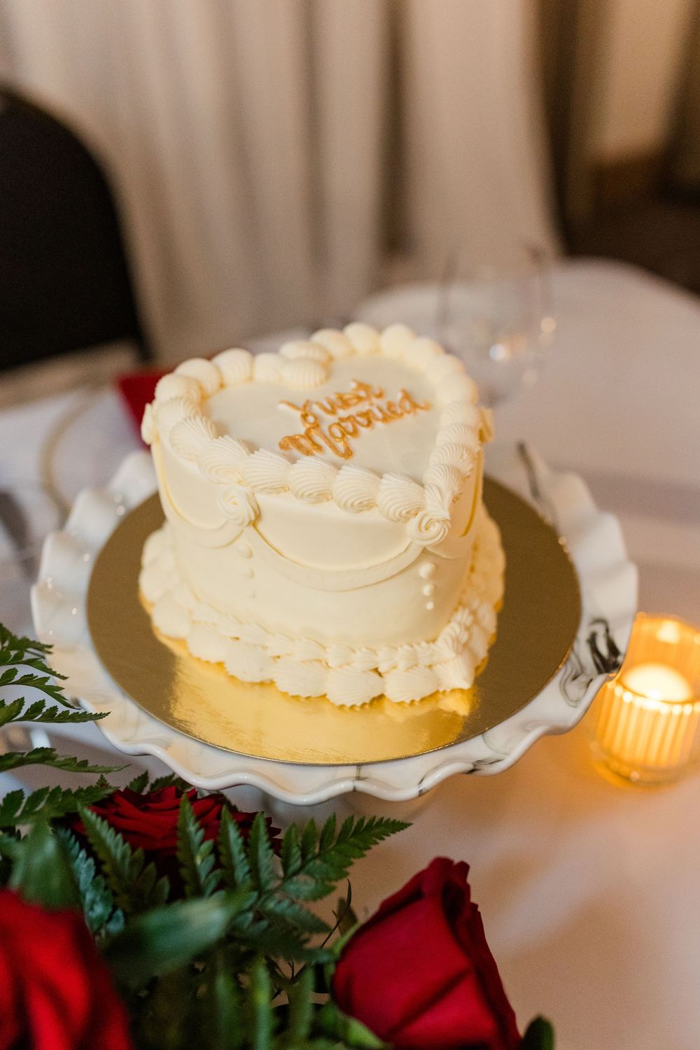 Four elegant white frosted cakes displayed on a table with candlelight and red roses creating a romantic atmosphere.