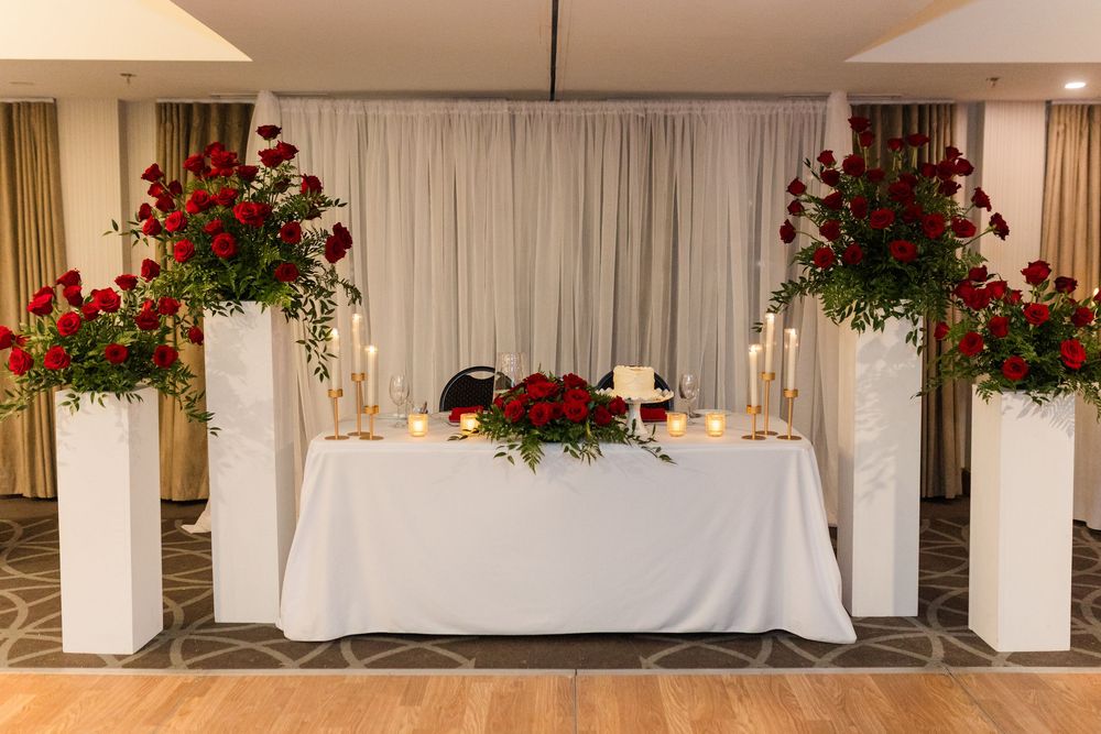 Elegant wedding reception hall with white tables and vibrant red floral arrangements hanging from columns.