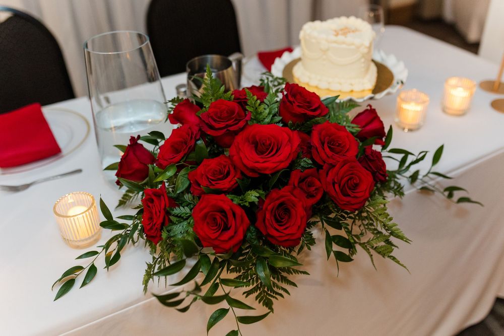 A romantic table setting with red rose centerpieces, white tablecloths, and glowing candles creates an elegant dining atmosphere.