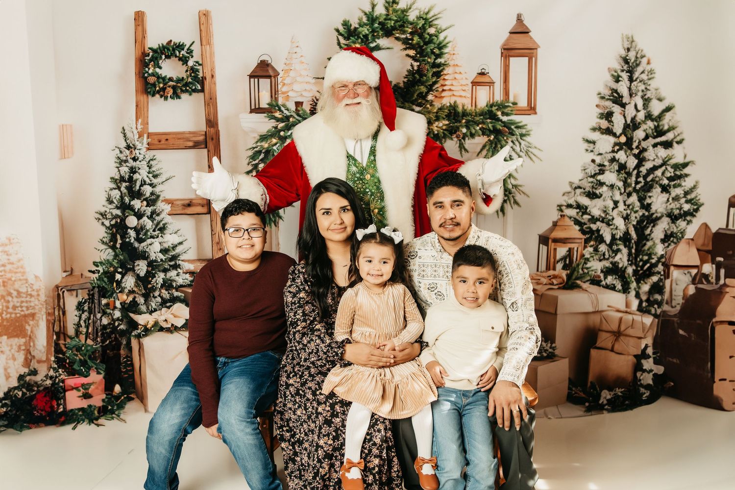 A group gathers in front of decorated Christmas trees and lanterns in a cozy white studio setting for holiday photos.