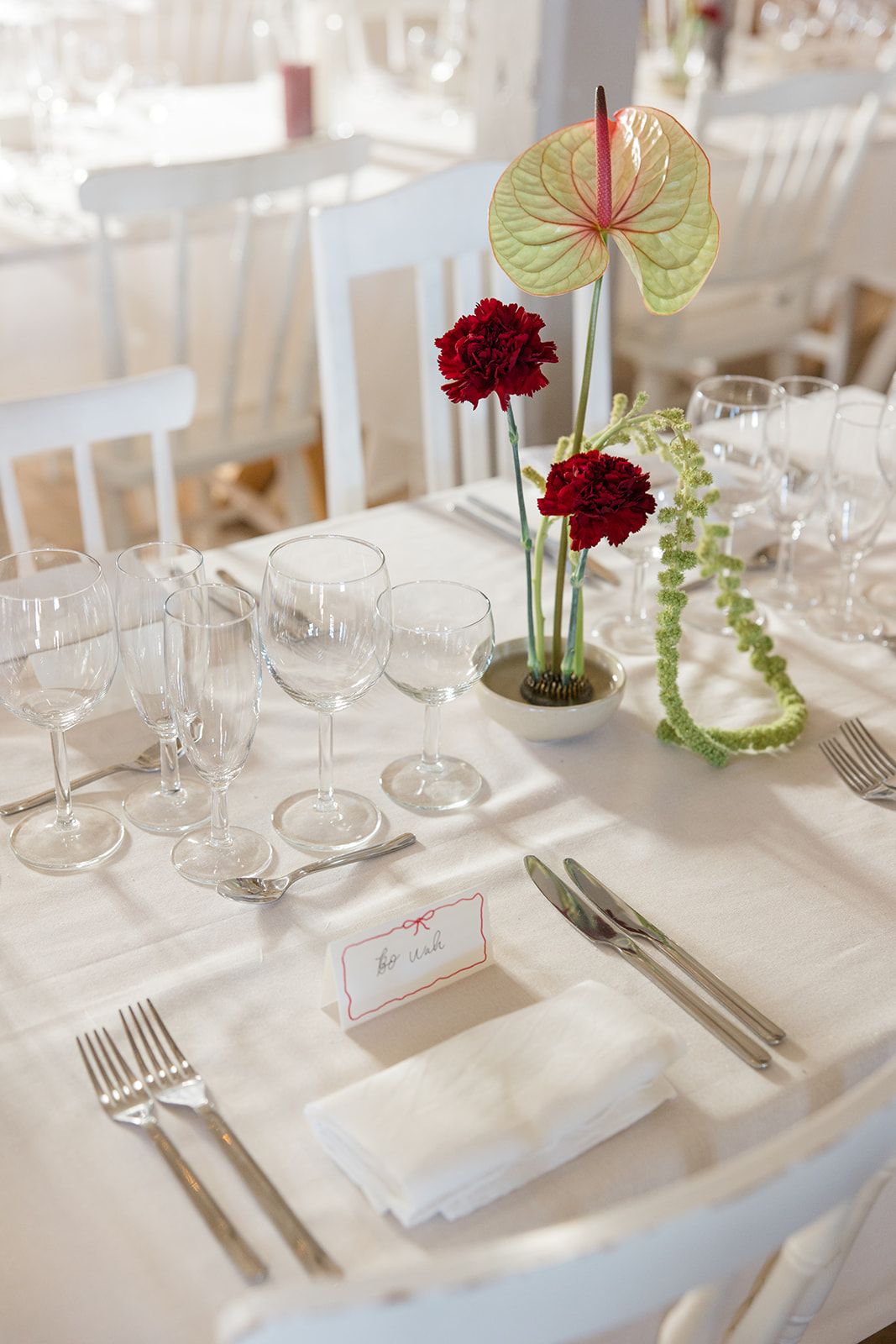 Elegant wedding table setting with red carnations, anthurium leaves, white linens and crystal stemware.