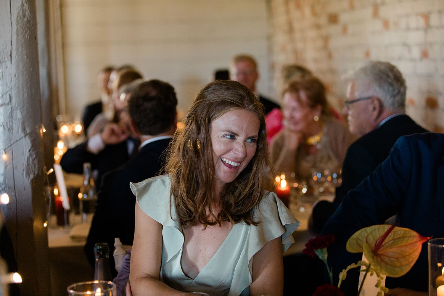 A candlelit wedding reception in a rustic brick-walled venue with guests mingling and dining at elegant tables.