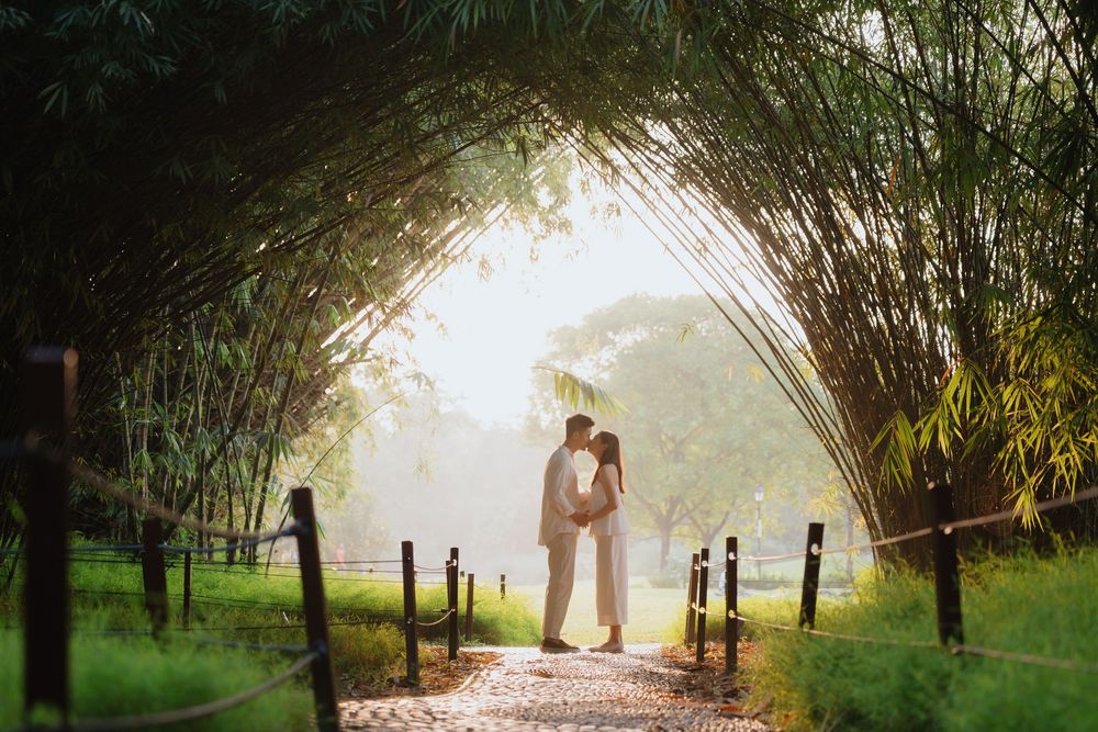 A romantic silhouette of a couple standing beneath an arched bamboo pathway during golden hour.