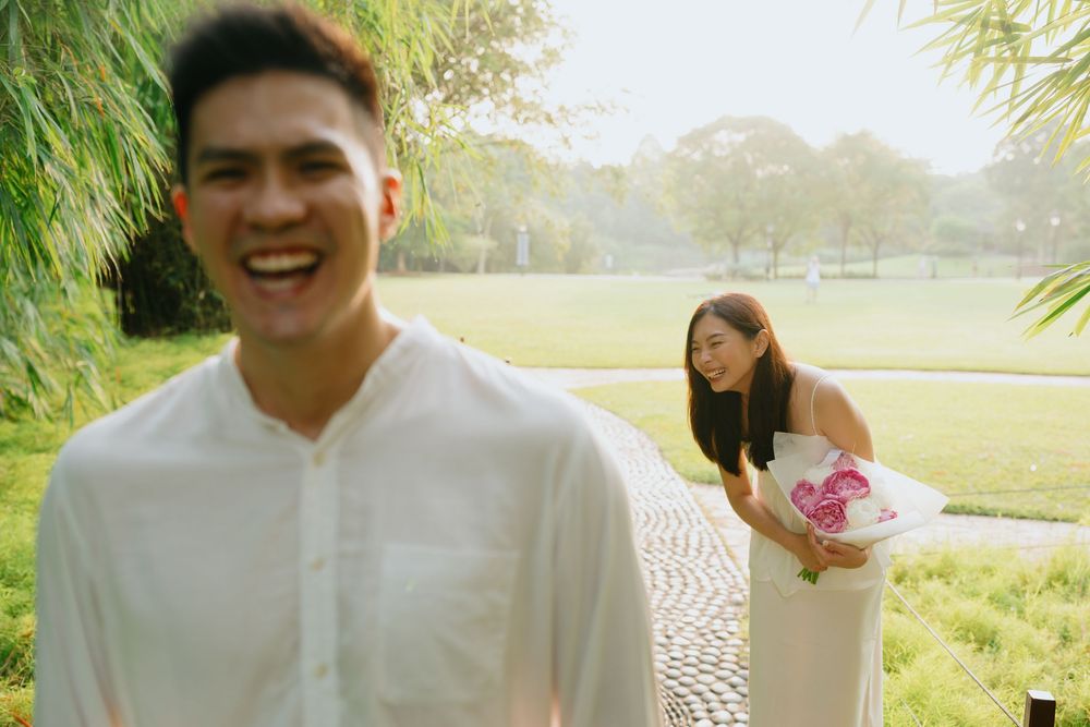 A couple poses together in an outdoor park setting during a sunny engagement photoshoot.