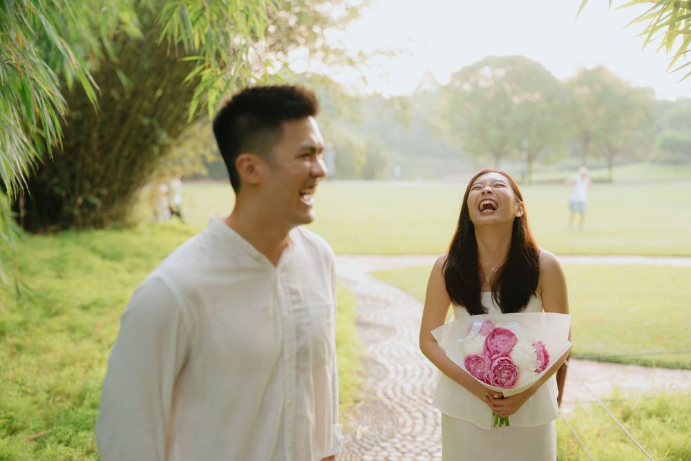 A couple shares joyful moments together during an outdoor engagement photo session in a sunlit park.