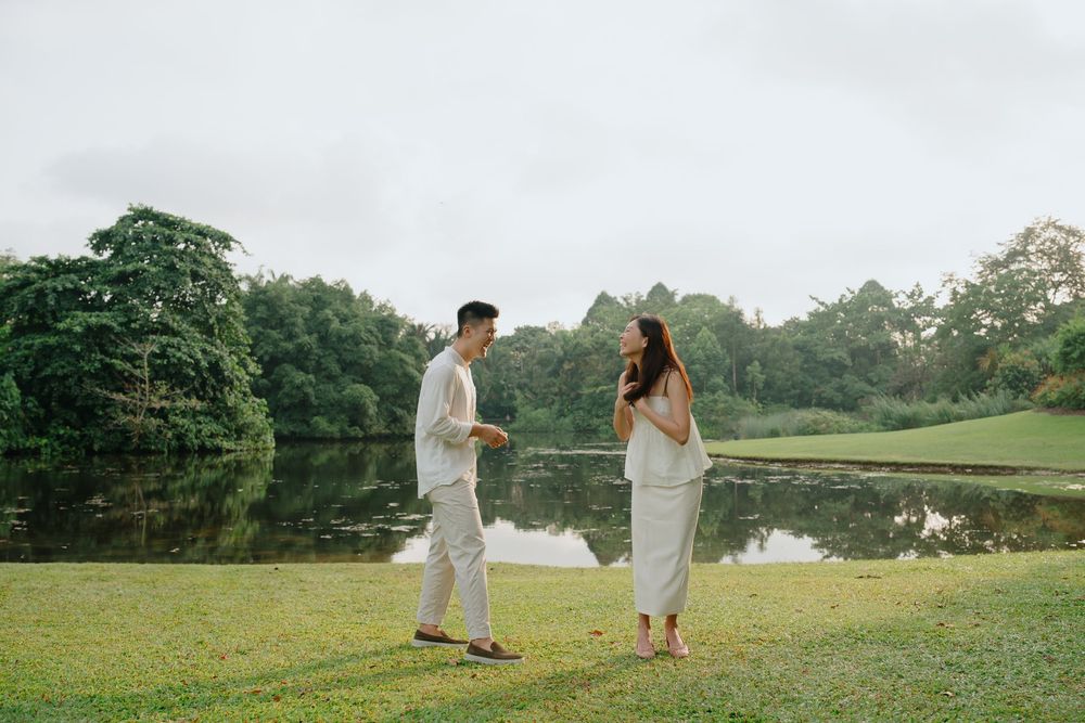 A couple in white outfits shares an intimate moment in a lush green meadow during an outdoor photo session.