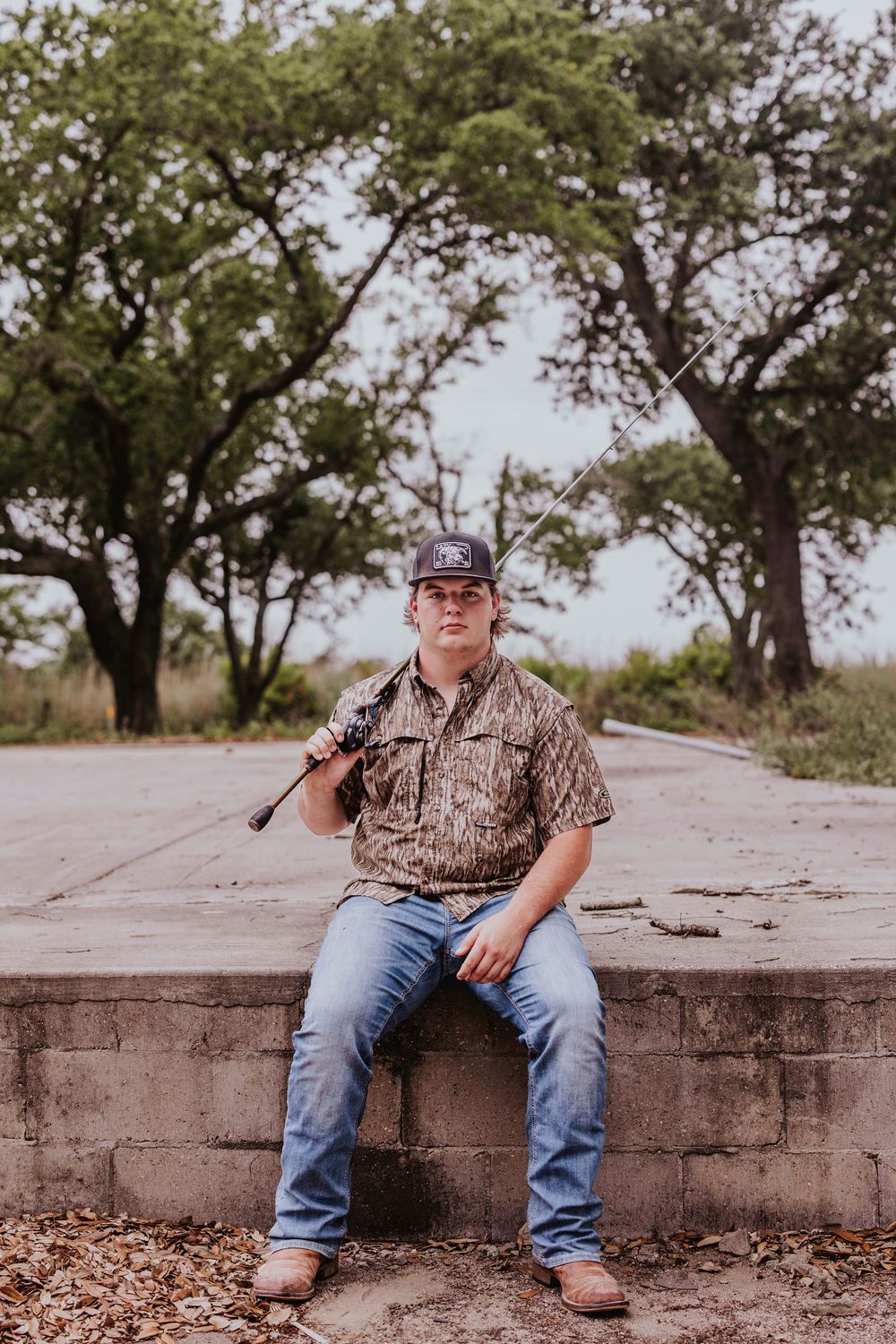 Person in hunting attire sits on concrete ledge in outdoor setting.