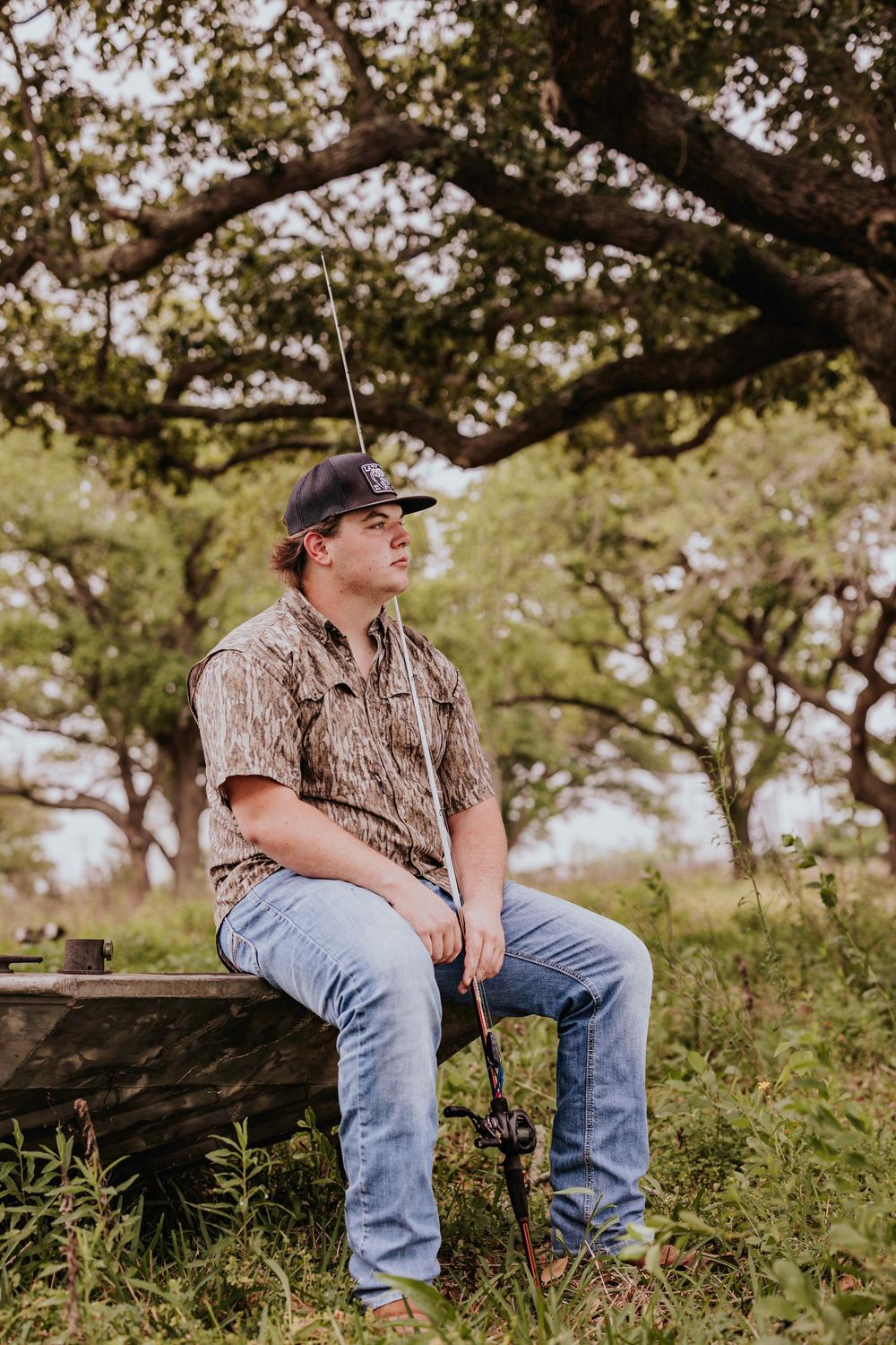 Person in camouflage shirt and jeans sits on wooden bench in outdoor rural setting.