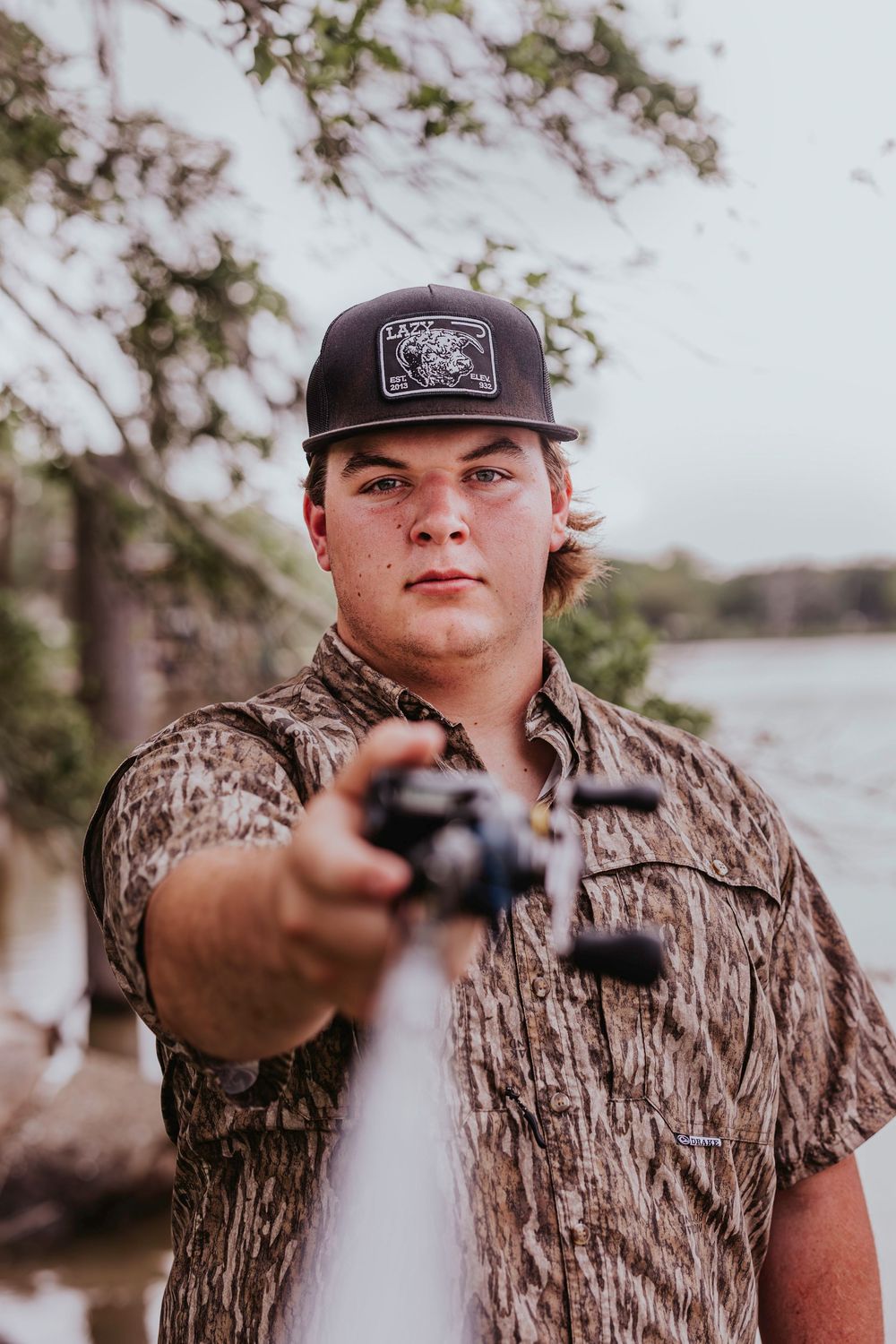 Person in camouflage clothing and baseball cap holding camera equipment outdoors.
