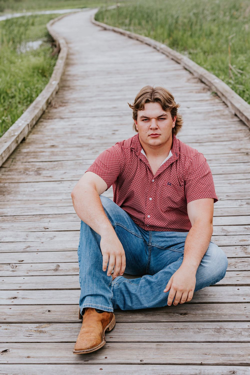 Casual portrait session on a wooden boardwalk surrounded by green grass.