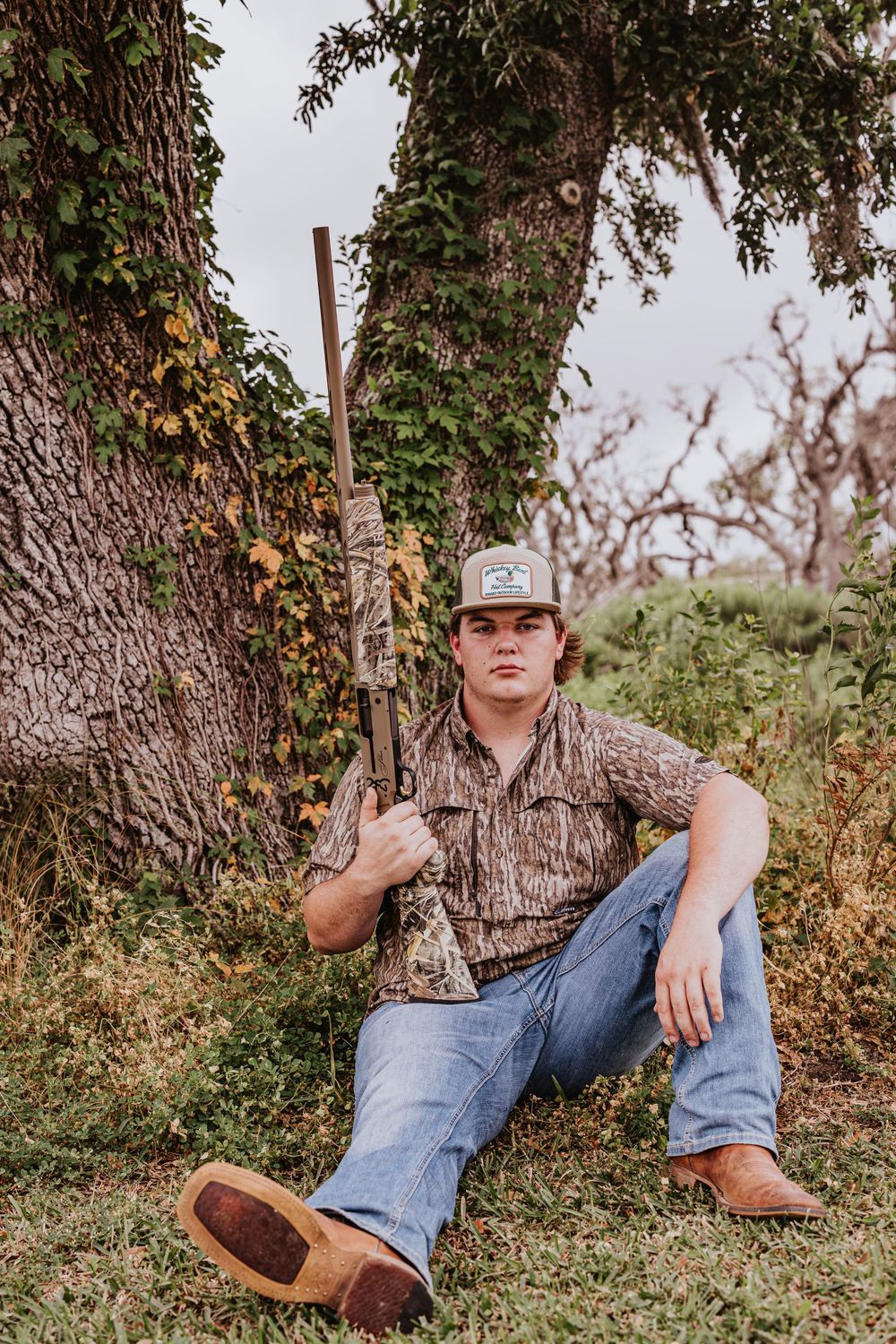 Person in camo shirt reclines against tree trunk in natural setting.