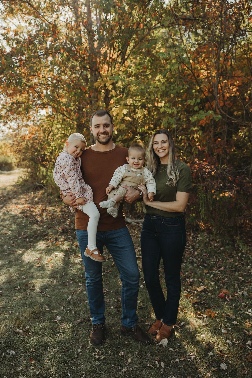 A family stands together against a backdrop of autumn foliage in a natural outdoor setting.
