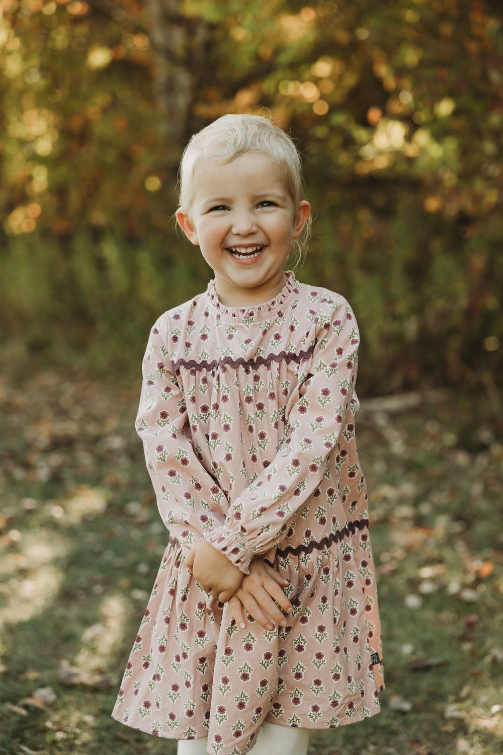 A child in a floral dress poses playfully outdoors in a series of candid autumn portraits.