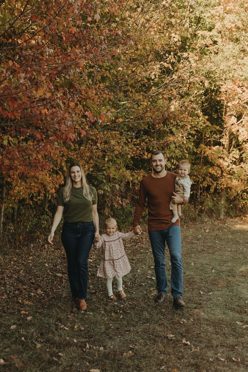 A family walks together through a scenic autumn forest setting with golden fall foliage in the background.
