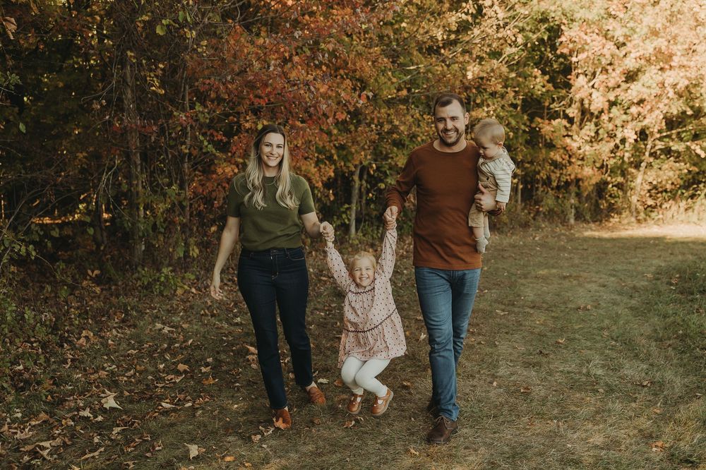 Family walking together on autumn path through colorful fall foliage in outdoor park setting.
