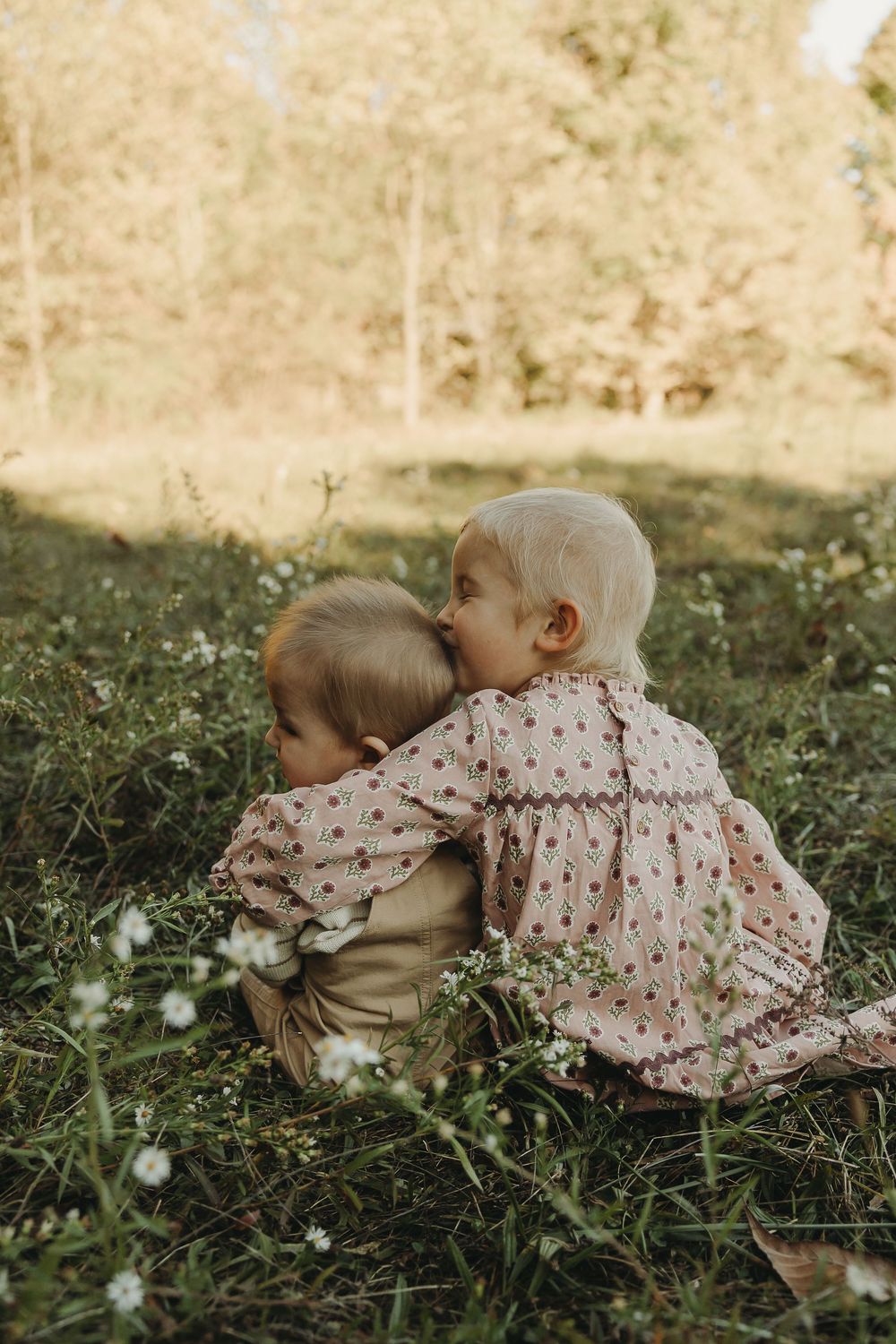 Two children in matching polka dot dresses lay together on grass in a sweet outdoor moment.