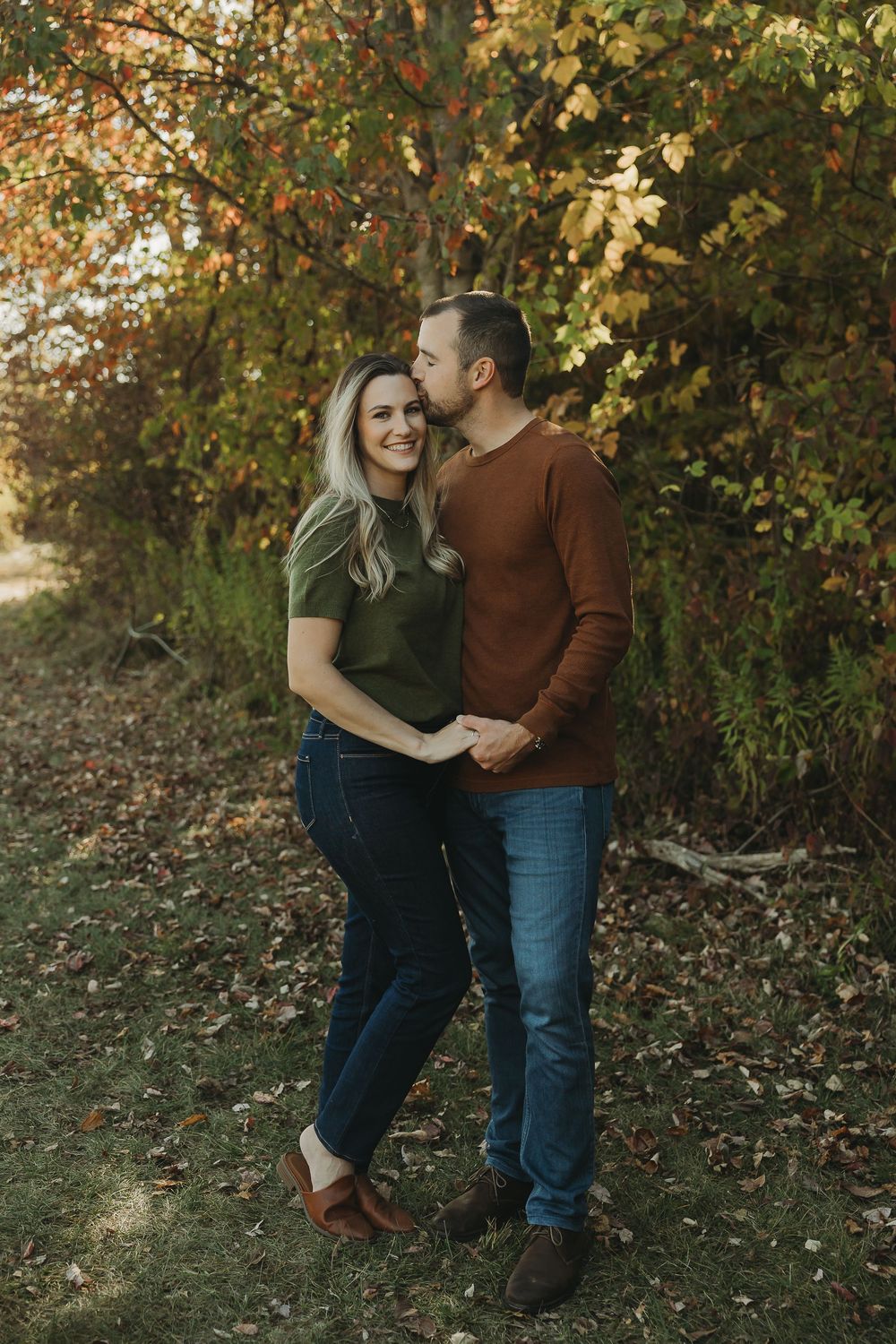 A couple shares tender moments together in a fall outdoor setting with golden leaves in the background.