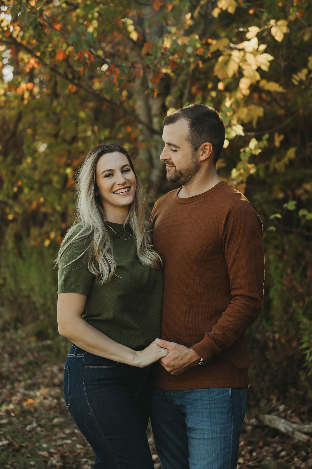 A couple shares a romantic moment together in a fall setting with golden leaves in the background.